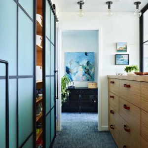 Primary Bedroom includes this walk-in closet with steel and glass sliding door panels on one side and built-in dresser with leather handles on the other.
