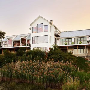 Coastal Modern Farmhouse Waterside Exterior. A contemporary design with wall-to-wall windows that frame breathtaking views of the estuary below.