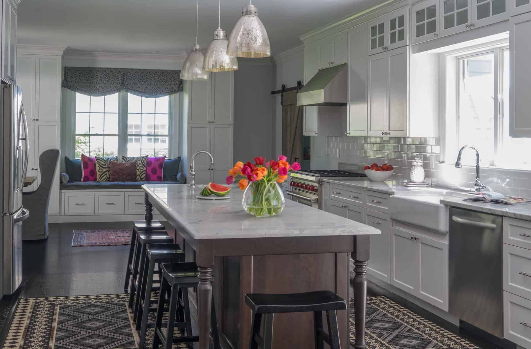 AFTER: The new kitchen island offers a stark color contrast to white cabinetry and establishes the farm table theme. Functionally, it provides ample seating. Cabinets were extended to ceilings with an upper row of interior lit transom cabinets. These maximize storage, given the high ceilings.