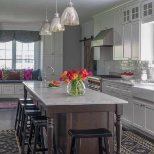 AFTER: The new kitchen island offers a stark color contrast to white cabinetry and establishes the farm table theme. Functionally, it provides ample seating. Cabinets were extended to ceilings with an upper row of interior lit transom cabinets. These maximize storage, given the high ceilings.