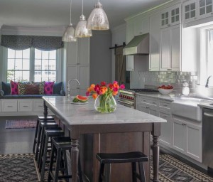 AFTER: The new kitchen island offers a stark color contrast to white cabinetry and establishes the farm table theme. Functionally, it provides ample seating. Cabinets were extended to ceilings with an upper row of interior lit transom cabinets. These maximize storage, given the high ceilings.