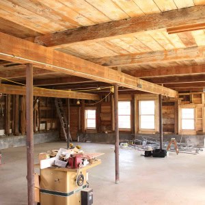 BEFORE: 1793 Barn Interior--Although the barn had a plywood ceiling from a previous renovation, a "hint" of timber-frame was exposed. The surprise discovered behind the ceiling was an expansive timber frame - oak tie beams that were 30' long, telltale hand tool marks, and other timber frame elements that indicated the barn predated 1800. (photo by Benjamin Nutter Architects)
