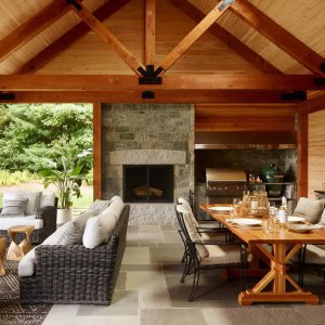 24-New-Addition-Outdoor-Room-Interior. The new space features an outdoor kitchen, a sitting area, radiant heated floors, a wood-burning fireplace, and a recycled solid granite block hearth. The exterior chimney for the new fireplace was a re-use of a brick chimney that was removed from the center of the interior of the house.