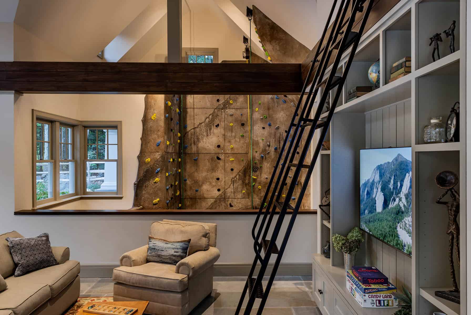 Poolhouse interior. A living space overlooks a 3 story climbing wall. Ladder leads to a sleeping loft overlooking the living space