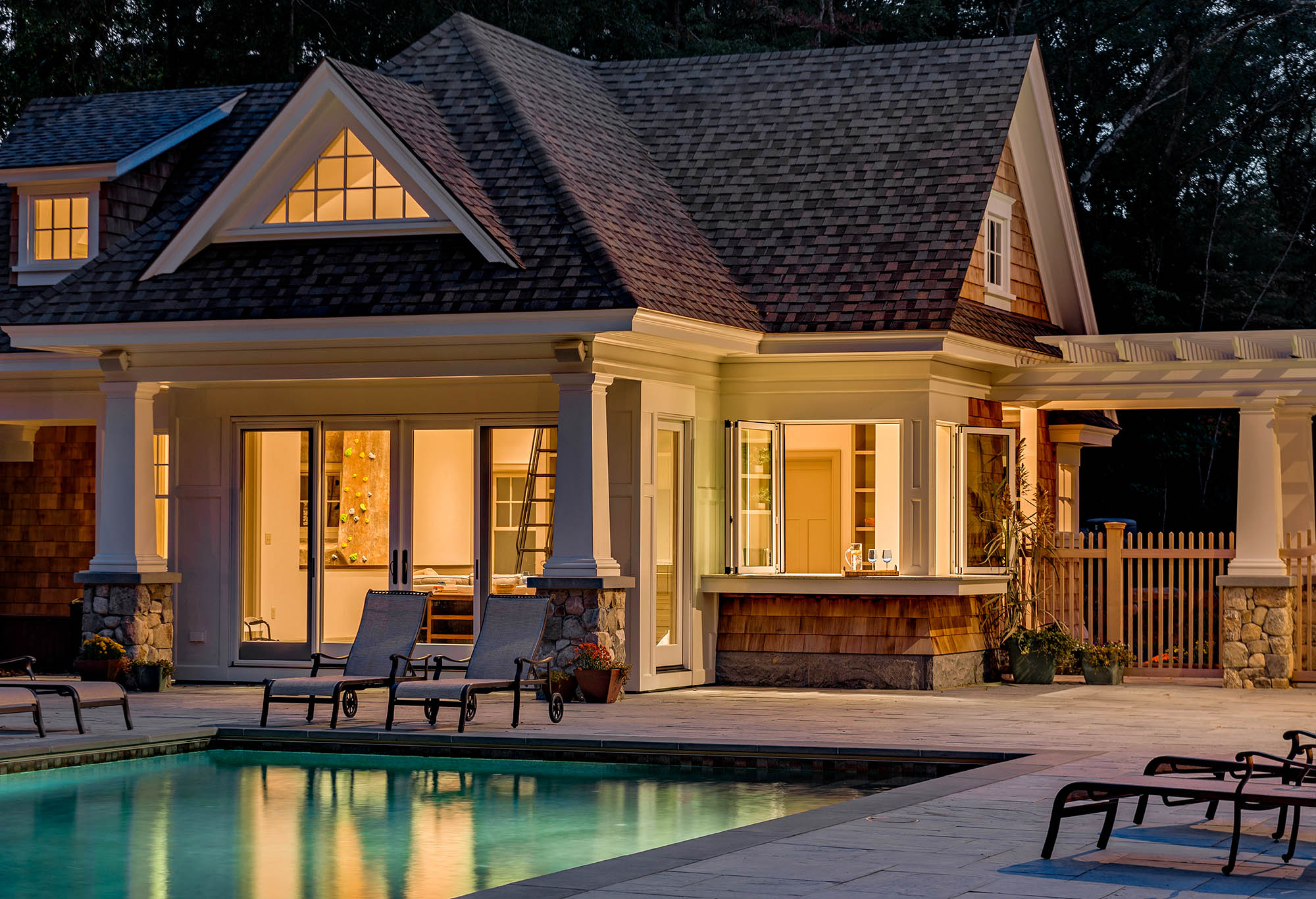 Cottage Style Pool House at Night, View of indoor climbing wall, Fully retracting bi-fold windows in the pool house kitchen allow for easy poolside food and drink service