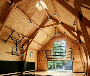 This residential indoor basketball court/fieldhouse features a structural Douglas Fir timber frame that is economical in design. While the frame supports a volume of space large enough to shoot a basketball from any angle, it uses smaller dimensioned timber sizes in a carefully thought-out design that makes efficient use of the timber to structurally support such a large space.